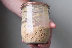 a person holding a glass jar with something in it's hand and some dirt on the bottom