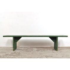 a green wooden bench sitting on top of a cement floor next to a white wall