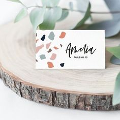 a place card sitting on top of a piece of wood next to some leaves and branches