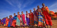 a group of people standing on top of a dirt field next to each other in colorful clothing