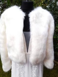 a white fur coat on top of a mannequin dummy in front of trees