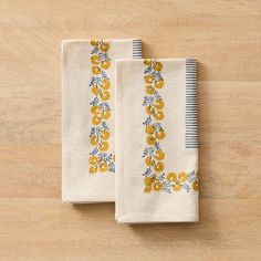 two white towels with yellow flowers on them sitting on a wooden table next to each other