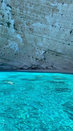 the water is crystal blue and there are rocks on the side of the mountain in the background