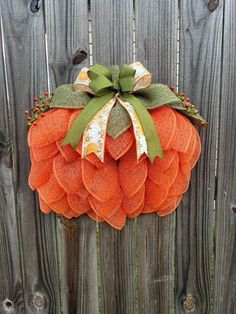 an orange mesh pumpkin with a green bow on it's head hanging from a wooden fence