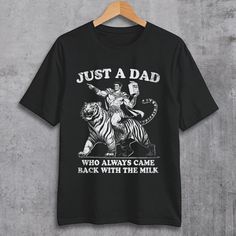 Surprise your dad with a touch of dark humor and vintage style! Our unique t-shirt features a bold, minimalist design of a strong dad triumphantly riding a big tiger while holding a cartoon of milk. Perfect for dads with a sense of humor, this shirt plays on the classic "went out for milk" joke with a twist. The retro-inspired artwork gives it a cool, vintage feel that any dad will love.  🌟Unisex Cotton T-Shirt *Medium fabric *Classic fit *Runs true to size *100% cotton *Tear-away label *Size u Retro Graphic Print T-shirt For Father's Day, Vintage Black T-shirt With Funny Text, Vintage Black T-shirt With Slogan, Retro Letter Print Tops For Father's Day, Father's Day Black T-shirt With Funny Print, Father's Day Black Graphic Print T-shirt, Retro Black T-shirt With Funny Text, Black Retro T-shirt With Funny Text, Retro Black Tops With Funny Text