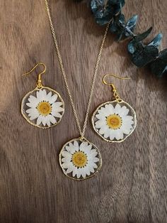 two necklaces with daisies on them are sitting next to some leaves and flowers