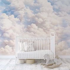 a white crib in front of a wall with clouds painted on it and a rocking horse