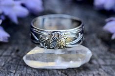 a silver ring sitting on top of a crystal block next to purple flowers and leaves