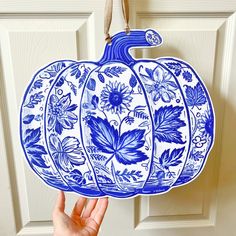 a hand holding up a blue and white pumpkin ornament with flowers on it