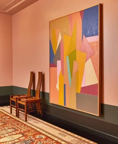 two wooden chairs sitting next to each other in front of a painting on the wall