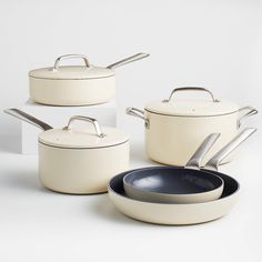 three pots and two pans on a white surface