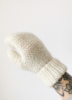 a person's hand wearing a white knitted mitten on top of their arm