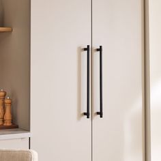 a tall white cabinet with black handles in a living room next to a chair and table