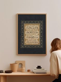 a woman sitting on a table in front of a wall hanging with an islamic calligraphy