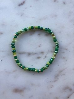 "Green Seed Bead with Gold Bracelet - great for stacking The beads measure 3mm. The knot is enclosed and hidden within a bead so you'll never see it poking through.  All bracelets are made for 7\" wrists (medium), but let me know if you need another size and I can easily adjust it for you!  Here's how to select the perfect size for your bracelet(s) : Measure your wrist using a soft measuring tape or a piece of string and a ruler. Then, size up approximately 1/2 inch for best fit. For example, a 6 inch wrist measurement sizes up 1/2 inch and orders a 6.5 inch bracelet. SIZING: X-Small: 6 inch Small: 6.5 inch Medium: 7 inch Large: 7.5 inch X-large: 8 inch Every bracelet comes with an individual organza jewelry pouch. All bracelets are handmade. If you would like something custom, please reac Organza Jewelry, Cash Budget Envelopes, Elastic Bracelet, Measuring Tape, Jewelry Pouch, The Knot, Seed Bead, Ruler, Seed Beads