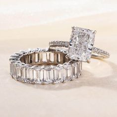 two diamond rings sitting next to each other on top of a white cloth covered surface