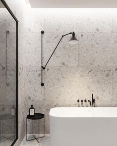 a white bath tub sitting next to a walk in shower and a black table with a lamp on it