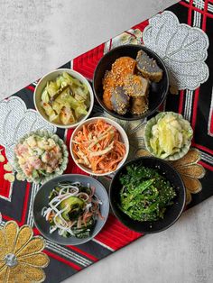 a table topped with bowls filled with different types of food next to a red and black place mat