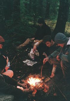 four people sitting around a campfire in the woods, one is lighting a candle