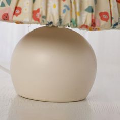 a white vase sitting on top of a table next to a lamp with a flowered shade