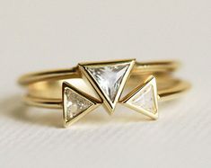 two gold rings with white diamonds in them on a white surface, one has a triangle shaped band and the other has three smaller triangles