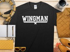 Elevate your wardrobe with this Wingman T-Shirt featuring a retro graphic design. Perfect for those who love to play the role of a supportive wingman, this funny tee is an excellent gift for friends or family members. The cool wingman design adds a touch of character to your casual outfits, making it a standout piece in your apparel collection.  The Gildan 5000 t-shirt features a medium-weight 100% cotton fabric with no side seams for a seamless fit. Enjoy the classic fit and family sizing optio Wingman Gifts, Retro Graphic Design, Navy Veteran, Design Cool, Design Graphique, Us Navy, Comfort Style, Environmental Impact, Funny Tees