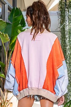 a woman standing next to a plant wearing an orange, pink and blue jacket with matching shorts