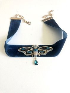 Art Deco necklace Cigale blue and gold with crystal drop on blue velvet ribbon: the necklace consists of a blue velvet ribbon 2.5 cm high, x 42 cm (with the chains, or 30 cm of velvet) on which is fixed a pretty golden metal cicada enamelled with blue and dotted with blue rhinestones. A small drop of turquoise blue crystal is hung under the cicada. The tape is attached by carabiner. Available as a pendant mounted on stainless steel chain, on sale separately in the shop: https://www.etsy.com/fr/l Necklace With Ribbon, Ribbon Necklace With Pendant, Blue Jewelry Aesthetic, Cristal Jewelry, Art Deco Outfit, Cicada Art, Cicada Necklace, Blue Velvet Ribbon, Velvet Accessories