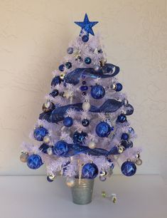 a blue and white christmas tree with ornaments on it's top, sitting in a silver pot