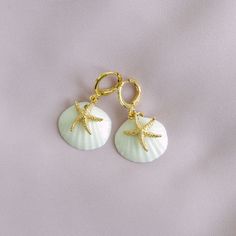 Embrace the ocean’s magic with these handcrafted porcelain shell and golden star earrings, inspired by the allure of mermaids and the deep sea. Available in both ear hook and clip-on versions, they’re perfect for channeling your inner sea goddess—friendly to any ear.   MATERIAL Handmade porcelain shells Gold-plated brass    SIZE & FIT 20mm x 35mm  COLOUR  White, gold  WEIGHT 5g/pair  Handmade in Denmark. Gold- or silver-plated colour will fade over time. This is a normal result from long-term wear and contact with air. However, with careful handling they can have a longer life. Here are some care tips for you:  Please avoid direct contact with water and chemical products, such as soap, perfume, hand cleaning gel, oils, make up, moisturisers, etc. Please do not wear jewellery while swimming Sea Goddess, August Birthstone Jewelry, Handmade Earring, July Birthstone Jewelry, Ocean Vibes, Handmade Porcelain, Porcelain Jewelry, Sea Star, Golden Star