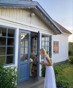 a woman in a white dress is opening the door to a house with a dog