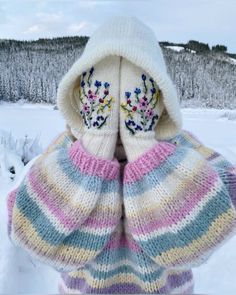 a person wearing mittens with flowers on them standing in the snow, covering their face