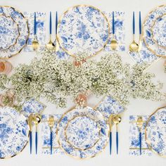 a table setting with blue and white plates, silverware, flowers and gold place settings