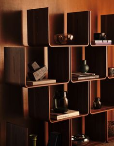 a wooden shelf filled with books and vases on top of each other in front of a brown wall