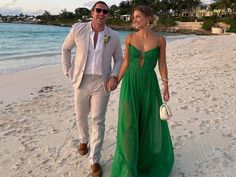 a man and woman in formal wear walking on the beach with their hand in each other's pockets