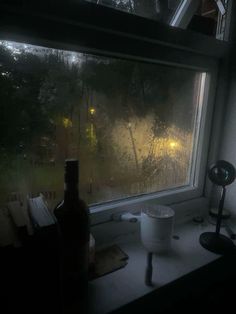 a window that has rain on it and a bottle in the window sill next to it