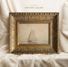 a painting with a sailboat on it in a gold frame sitting on a white sheet