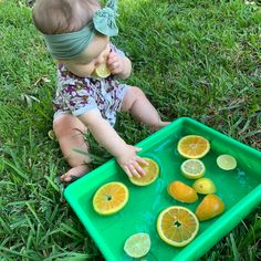 a baby sitting in the grass with lemons and oranges on it's tray