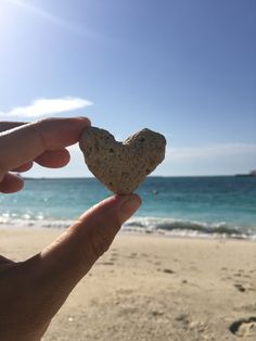 a person holding up a heart shaped rock on the beach