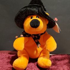 a teddy bear with a black hat and scarf on it's head sitting on a pink blanket