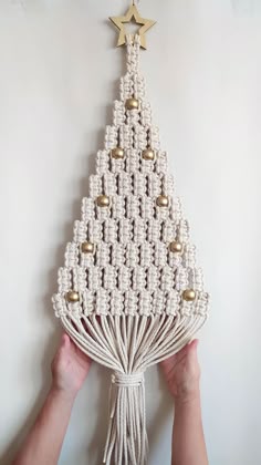 someone is holding up a christmas tree made from macrame beads and gold bells