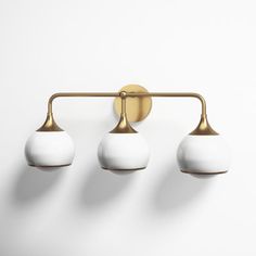 three white balls are hanging from a brass wall light with four lights on each side