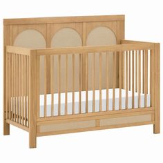 a wooden crib with white sheets on the bottom and beige linens around the sides