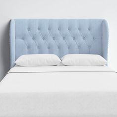 an upholstered bed with white pillows and blue headboard