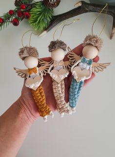 three handmade christmas ornaments hanging from the palm of a person's hand, with pine cones and evergreen branches in the background