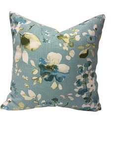 a blue pillow with white and green flowers on the front, sitting on a white background