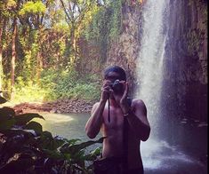 a man standing in front of a waterfall holding a camera to his face while taking a photo