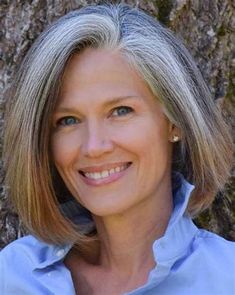 a woman with blonde hair and blue shirt standing in front of a tree smiling at the camera