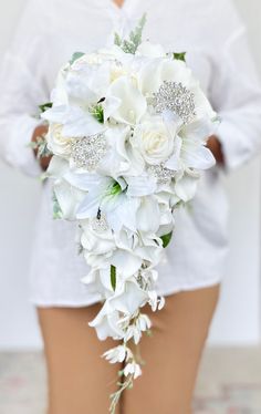 "This beautiful white cascading bouquet is one our our luxurious, high quality bouquets. It is made out real to touch roses, real touch calla lilies, real touch lilies, a spray of silk orchids, silk hydrangeas and a touch of dusty miller. The floral used in this bouquet   feel just like real flowers. This bouquet can also can be arranged with or without shimmering rhinestone brooches. Perfect for your white, minimalistic, or modern wedding!   Dimensions: Measures 10\" across and cascades 23\" long WITH the brooches and 9\" x 23\" WITHOUT the brooches. If you are interested in a bouquet that is a different size or shape for your bridesmaids, please send me a message so that I can accommodate your request.   VISIT MY SHOP  https://www.etsy.com/ca/shop/AdoredOccasions?ref=hdr_shop_menu Check Bridal Bouquet Orchids And Greenery, Calla Lily And Tulip Wedding Bouquet, Bridesmaid Floral Bouquet, Long Wedding Bouquets Brides, Wedding Bouquet Calla Lily, Teardrop Wedding Bouquet, White Snapdragon Bouquet, Bride White Bouquet, Orchid And Hydrangea Bouquet