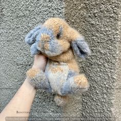 a hand holding a small stuffed animal in front of a wall